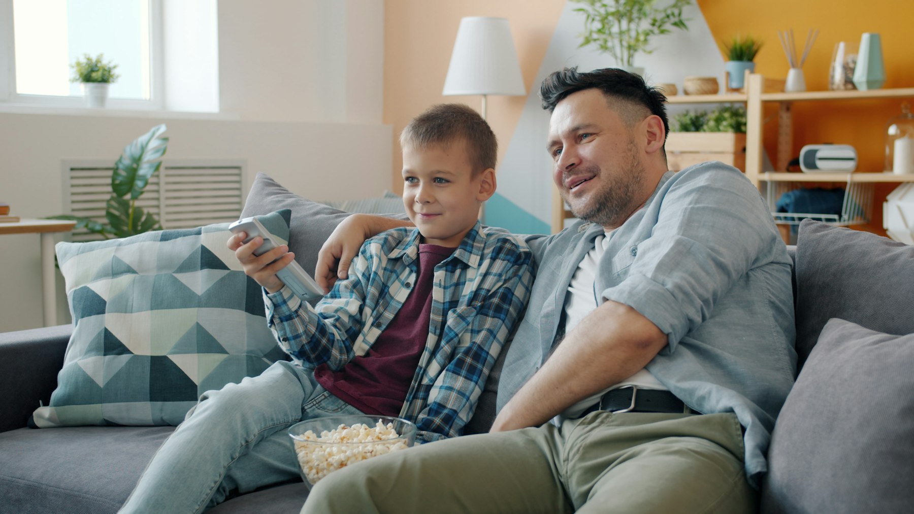 A father and son watching television together on the sofa